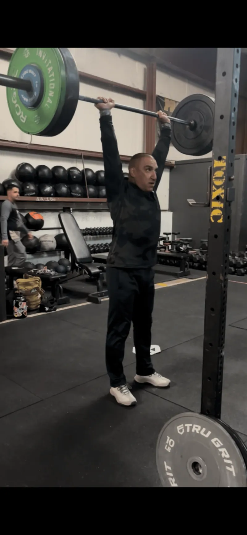 A Toxic Fitness athlete locking out a barbell overhead at the squat rack